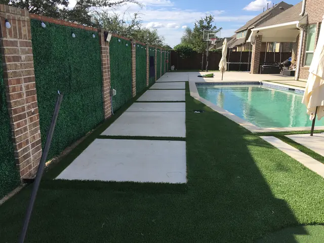Brick columns carrying a screen along a property line, with large set pads running through artificial turf beside a pool