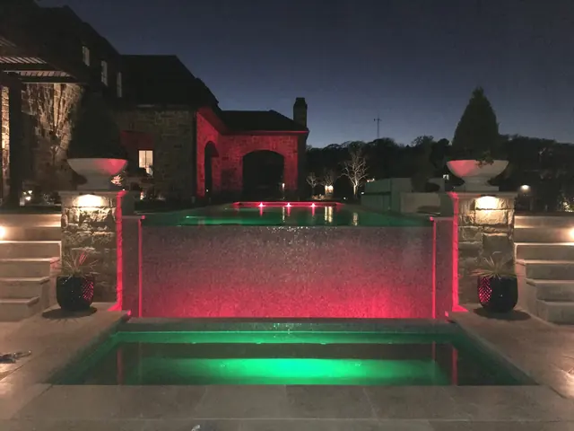 A raised wall spilling water into a lit pool between stone columns with planted bowls on top, and steps down either side