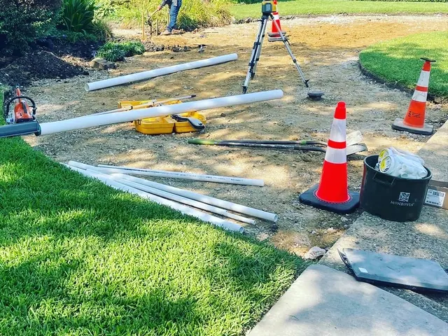 The same yard closer in: pipe laid out across the graded area beside a level, a tool case and traffic cones, with the new sod edge running past