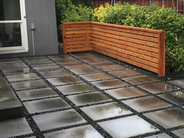 A horizontal cedar slat screen built along the edge of a paved patio, screening a planted bed behind it