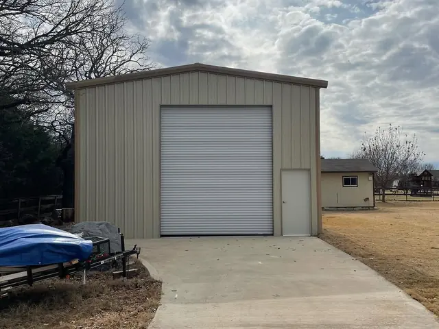 A new concrete apron running from a metal shop building out towards the yard, with the roll-up door open onto it