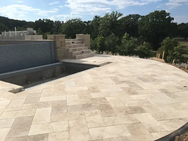 A travertine pool deck laid in a French pattern on a rural lot, with a raised wall along the far side of the pool and cut stone steps down onto the deck