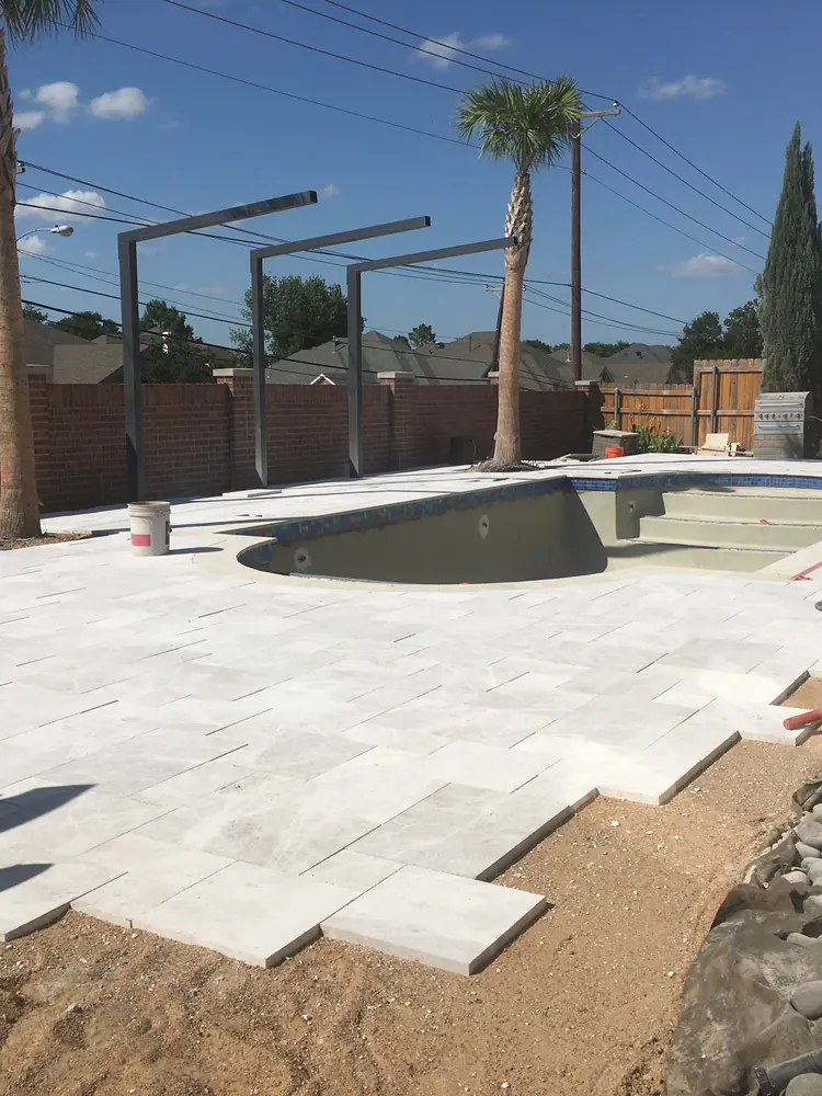 A pool deck being laid, seen upright: pavers set out from the water with bare bedding where the next courses go